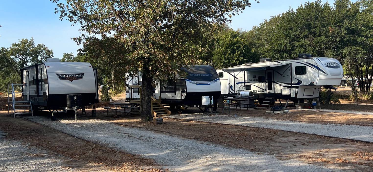Three travel trailers parked on shaded sites at Hog Mountain RV Ranch in late afternoon light